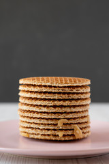 Stack of homemade Dutch stroopwafels with honey-caramel filling on pink plate, side view. Close-up.