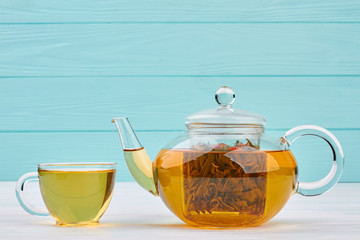 Cup of hot tea and a teapot. Glass teapot and cup of tea on blue background. Tea culture concept.