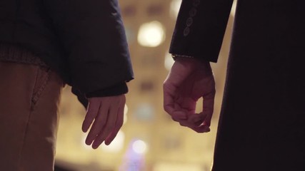 Couple of two males wearing winter clothes, they are holding hands standing outside in cold winter street in the evening.