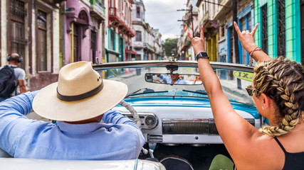 Havana Cuba. Woman smiling happy enjoying car road trip travel vacation, holding hands up in blue vintage convertible car on the colourful streets of Havana.