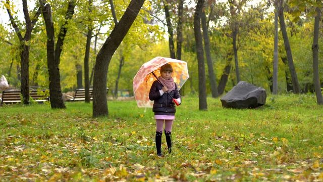 little girl rotates an umbrella in autumn park