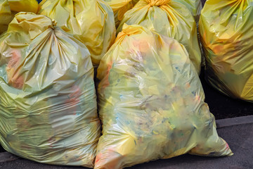 Yellow plastic trash bags. Recyclable garbage consisting of glass, plastic, metal and paper at side...