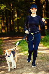 Girl walking with beagle dog outdoors in nature on a path in forest.