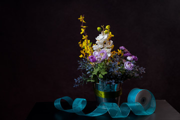 White and yellow flowers in a pot. With a blue ribbon at the bottom. On black background.