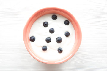 White yogurt with blueberry inliving coral color bowl on white wooden table. Free copy space for text. 