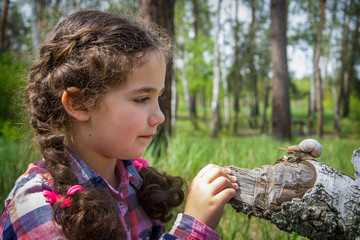 In the summer in the woods a little girl examines a snail.