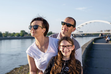 Happy family of three enjoying view over the river at sunset.