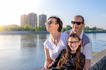 Happy young family of three sitting on the river embankment