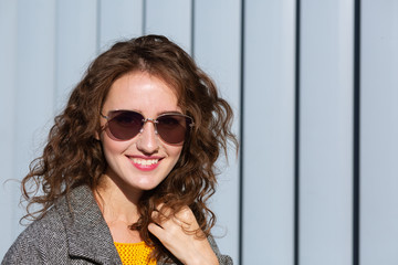 Urban portrait of merry brunette girl wearing sunglasses, posing near the shutters. Space for text