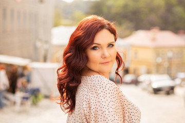 Stylish red haired middle-aged woman with curly hair walking at the city. Space for text