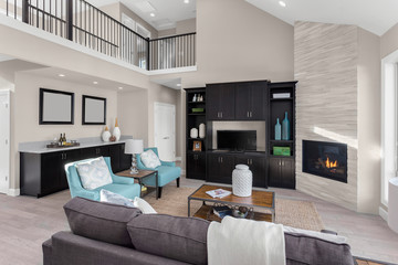 Living room with tall ceiling, fireplace, tv, and hardwood floors in elegant new home