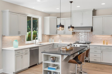 Kitchen in new elegant home with island, pendant lights, and stainless steel appliances