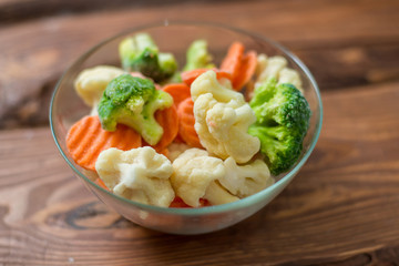Fresh frozen sliced vegetables - cabbage, carrots in a plate on a wooden background.
