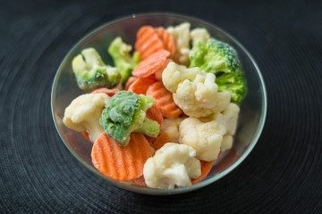 Fresh frozen sliced vegetables - cabbage, carrots in a plate on a black background.