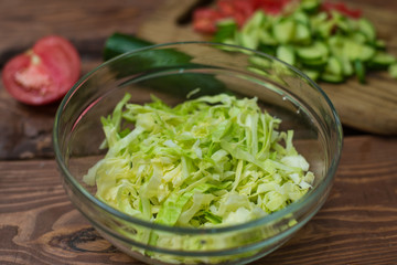 Chopped fresh green cabbage in a glass bowl on a wooden background. Cooking healthy, healthy, vegetable salad.