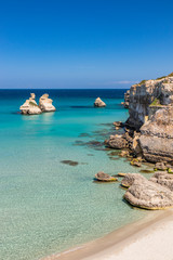 The bay of Torre dell'Orso, with its high cliffs, in Salento, Puglia, Italy. Turquoise sea and blue sky, sunny day in summer. A beach of fine white and pink sand. The stacks called the Two Sisters.