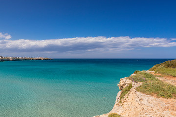 The bay of Torre dell'Orso, with its high cliffs, in Salento, Puglia, Italy. Turquoise sea and blue sky, sunny day in summer. Panorama of the sea on the horizon and houses on the reef.