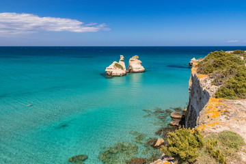 The bay of Torre dell'Orso, with its high cliffs, in Salento, Puglia, Italy. Turquoise sea and blue sky, sunny day in summer. The stacks called the Two Sisters. A person swims in the clear water