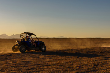 Unrecognizable people driving buggy during safari trip at sunset in Arabian desert not far from the...