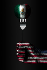 A hand with a drawn USA flag holds a fork, on which is a ball with a drawn Mexico flag, a sign of...
