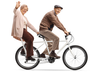 Senior woman and man riding a tandem bycicle and waving