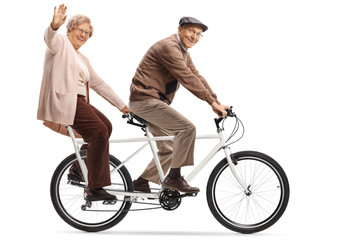 Obraz premium Senior woman and man riding a tandem bycicle and waving