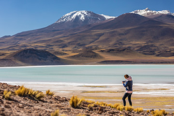 Landscape woman photographer taking mobile phone photos in an amazing wilderness environment at Atacama Desert Andes mountains lagoons. A woman cut out silhouette over the awe Tuyajto Lagoon scenery