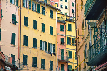 Fototapeta na wymiar facade of yellow and pink houses of Riomaggiore with green windows with wooden shutters and balconies , Cinque Terre, Liguria, Italy