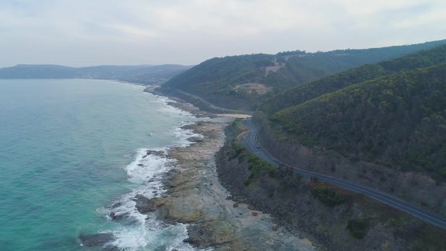 Drone flight over cars driving on a winding narrow road near ocean coastline