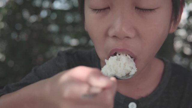 4k follow up Young Asian Thai boy take a spoon of rice in to his mounth during lunch in a garden under a natural light