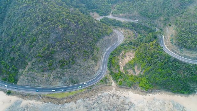Tracking aerial shot of cars driving on a narrow coastal highway in Australia