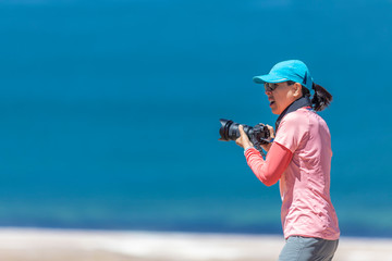 Landscape woman photographer taking photos in an amazing wilderness environment at Atacama Desert Andes mountains lagoons. A cut out silhouette over the blue waters with a mirror less camera shooting