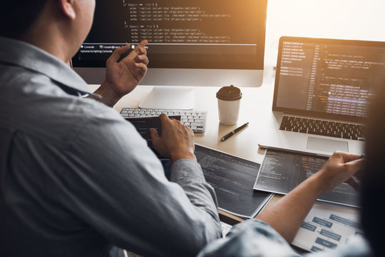 Two software developers are using computers to work together with their partner at the office desk.
