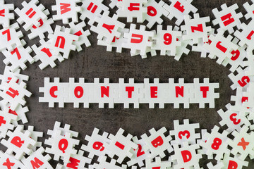 Content is king in advertising or creative communication concept, white puzzle jigsaw building the word content on dark black cement surrounded by other alphabets