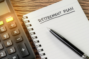 Retirement plan concept, calculator with empty notepad with pen and handwriting headline as Retirement Plan on wood table, plan of saving and investment for expense after retire life
