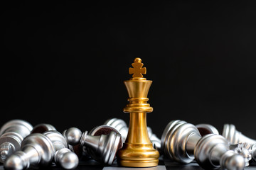 Gold king chess piece win over lying down silver pawn on black background