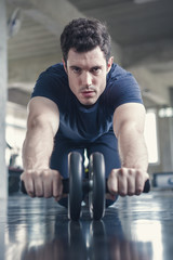 Athlete sporty man doing exercise with abs roller wheel to strengthen his abdominal muscle in gym