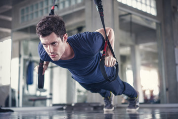 Athlete sporty man doing exercise with fitness trx straps to strengthen his abdominal muscle in gym