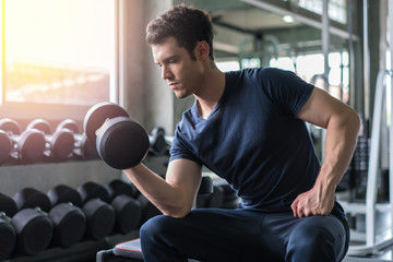 Handsome weightlifter lifting bench press working out with dumbbell in the gym