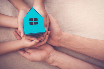 Adult and child hands holding blue paper house for family home and homeless shelter, social...