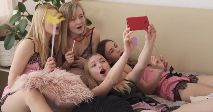 Girl friends taking selfie while posing with fake props on bed
