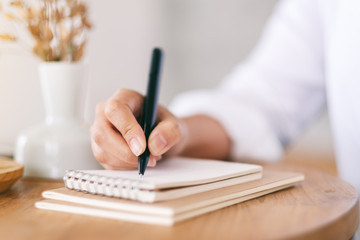 Closeup image of a woman writing on a blank notebook on wooden table