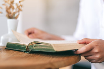 Closeup image of a woman holding and reading a vintage novel book on wooden table