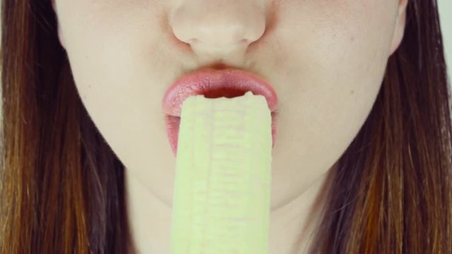 Woman sexually eats a banana. Close-up, light background
