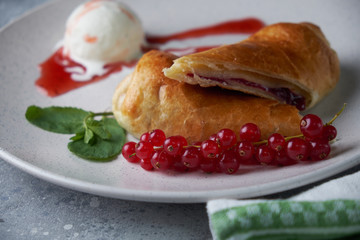 Sliced homemade berry strudel served with fresh red currant berries and powdered sugar on an old background on a plate with ice cream
