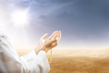 Muslim man praying with prayer beads on his hands in desert