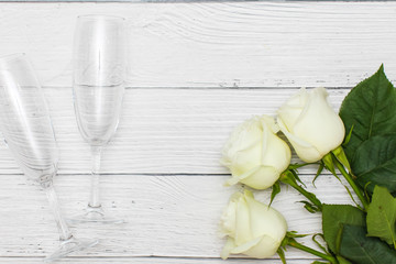 top view of three White roses and two champagne glasses on old white wooden table love concept.