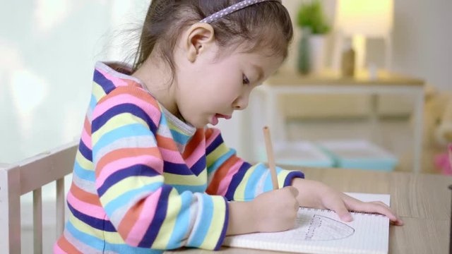 Close up shot asian little girl writing and drawing a notebook on the wooden table at home, Educational concept for school