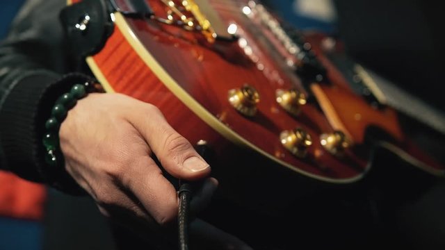Musician connects the jack cable to the electric guitar, guitar bracelet on hand.