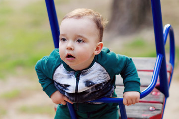 One-year-old boy plays on a playground next to a slide. He is smiling.